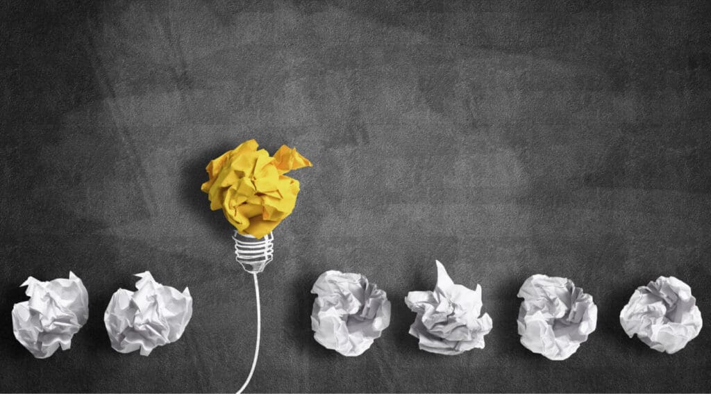 Blackboard with seven paper crushed balls one is rising as yellow paper crushed lightbulb whilst other white balls are static