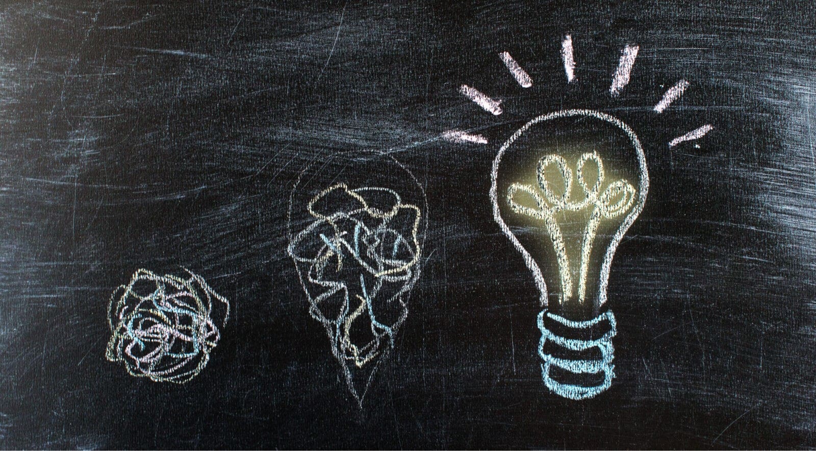 blackboard showing idea development from crushed ball to growing shape to glowing lightbulb all in pastel chalk colours