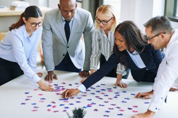 colleagues gathered around a white table looking and moving jigsaw pieces in bright colours