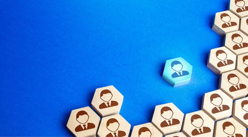 Bright blue background with group of hexagon wooden shapes with people heads with one hexagon separated standing out in blue