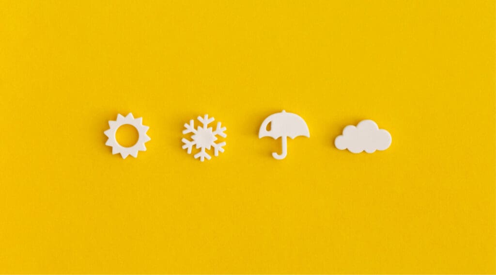 bright yellow background with four white 3-D icons of weather sun snowflake umbrella and cloud in straight horizontal line