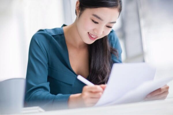 woman smiling sitting at desk with paper and pen posed to write