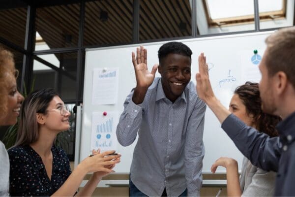 Corporate team meeting working on project using white board celebrating with smiles and high fives